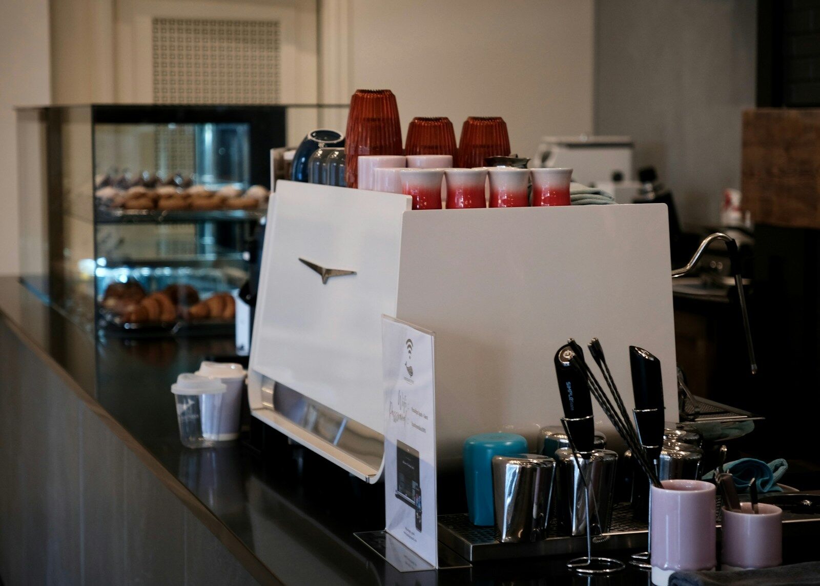 Espresso machine with cups and pastries in background.